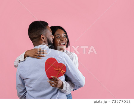 Affectionate black couple with Valentine's Day gift embracing on pink studio background, copy space 73377012