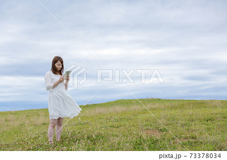 草原でタブレットpcを操作する女性の写真素材