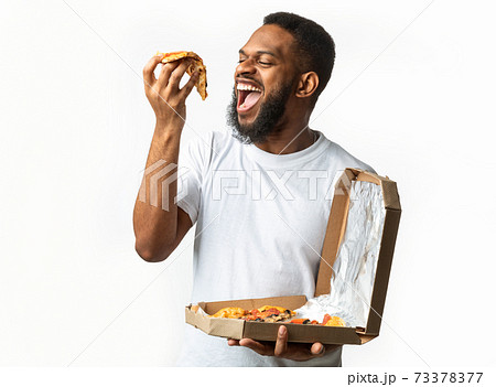 Hungry Black Guy Eating Pizza Slice Standing Over White Background 73378377