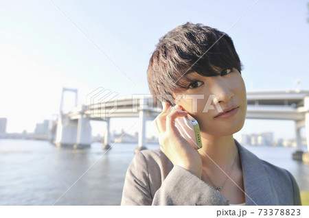 レインボーブリッジをバックにスマートフォンで話す女性 73378823
