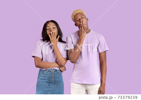Tired black couple yawning with hands near mouths, feeling sleepy on lilac studio background 73379239