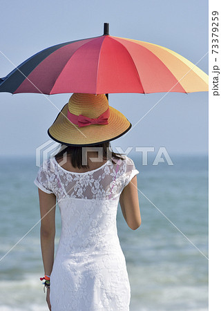 海辺で虹色の傘をさす女性の後ろ姿の写真素材