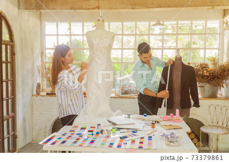 Two Asian fashion designers adjusting dress on model in the studio Two Asian fashion designers adjusting dress on model in the studio 73379861