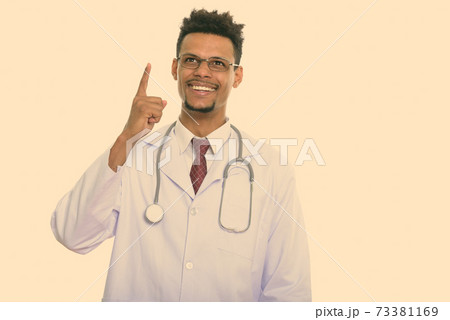 Thoughtful happy African man doctor smiling while pointing finger up 73381169