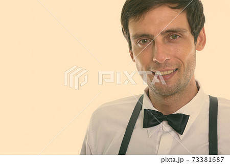 Close up of young happy man smiling while wearing suspenders and bow tie 73381687