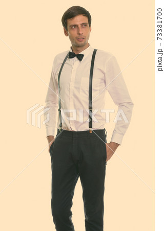 Studio shot of young handsome man standing and thinking while wearing suspenders and bow tie 73381700