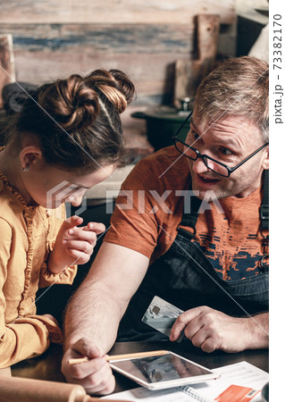 Father with daughter with credit card shopping online in a grocery store. Life style photography. Home kitchen. Food Delivery Service. Vertical shot Father with daughter with credit card shopping online in a grocery store. Life style photography. Home kitchen. Food Delivery Service. Vertical shot 73382170