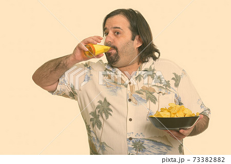 Fat Caucasian man drinking beer and holding bowl of chips ready for vacation 73382882