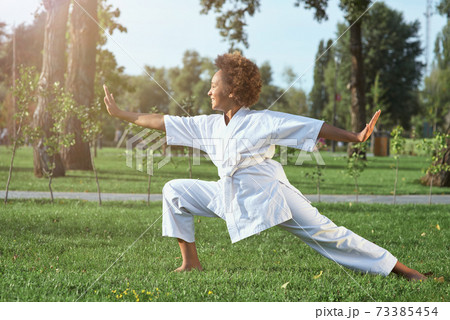 Adorable Afro American girl practicing karate on sunny day in park Adorable Afro American girl practicing karate on sunny day in park 73385454