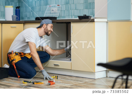 The plumber you can count on. Full length shot of cheerful young plumber wearing tool belt smiling while examining a sink before fixing it in the kitchen The plumber you can count on. Full length shot of cheerful young plumber wearing tool belt smiling while examining a sink before fixing it in the kitchen 73385502