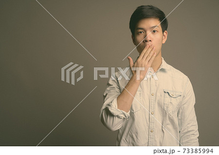 Young handsome Asian businessman wearing white shirt against gray background 73385994