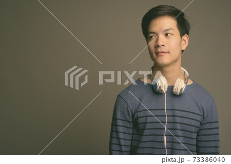 Young handsome Asian man wearing headphones against gray background Young handsome Asian man wearing headphones against gray background 73386040
