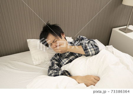 ベッドルームにてパジャマ姿でくしゃみをする男性 73386364