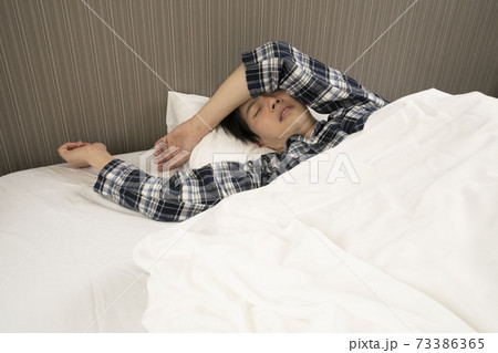 寝起きに発熱がわかり、体調が悪くなって会社に行けないパジャマ姿の男性	 73386365