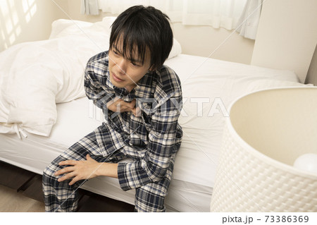 昨日の飲み会が遅くまで続き、朝胸焼けが酷く起きれないパジャマ姿の男性 昨日の飲み会が遅くまで続き、朝胸焼けが酷く起きれないパジャマ姿の男性 73386369