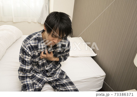 昨日の飲み会が遅くまで続き、朝胸焼けが酷く起きれないパジャマ姿の男性 73386371