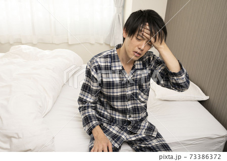 寝起きに発熱がわかり、体調が悪くなって会社に行けないパジャマ姿の男性 寝起きに発熱がわかり、体調が悪くなって会社に行けないパジャマ姿の男性 73386372