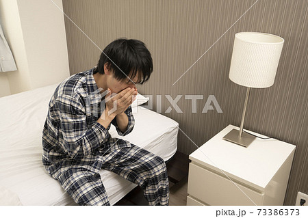 ベッドルームにてパジャマ姿でくしゃみをする男性 73386373