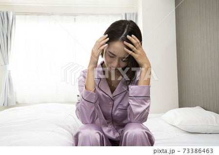 病気で寝込んでいる女性/体調の悪い女性/ベットに寝ている美しい女性/ベッドに座っている美人 73386463