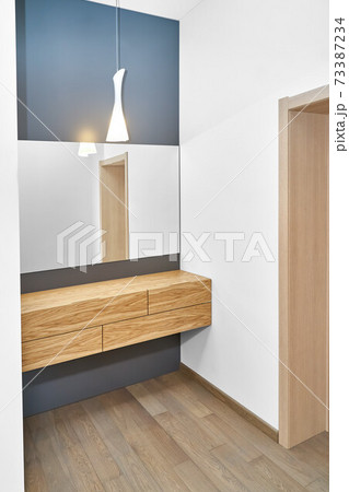 Floating cabinet of natural timber under large mirror in room 73387234