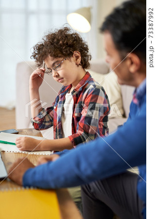 For better future. Thoughtful little latin school boy doing homework together with his father, writing on the paper while sitting at the desk at home 73387992