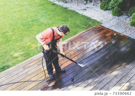 man cleaning terrace with a power washer - high water pressure cleaner on wooden terrace surface 73390662