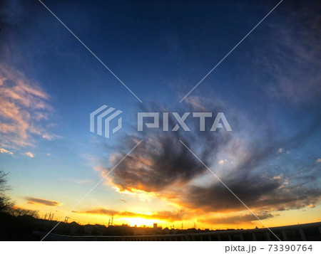 青い空に浮かぶ灰色の雲と日没の夕焼けが見える街並みのシルエットがある風景 73390764