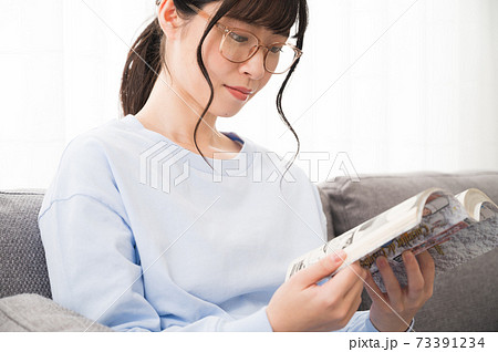 ソファーでコミックを読む眼鏡の女性 73391234