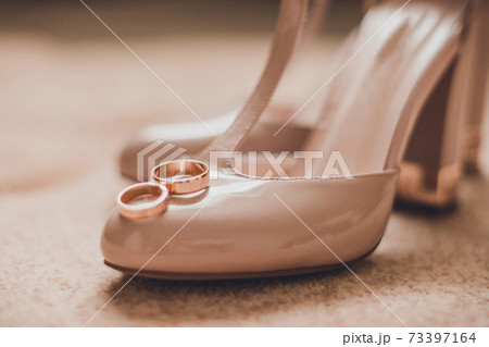 Beautiful pair of bride's shoes with wedding rings, glare from the surface. 73397164