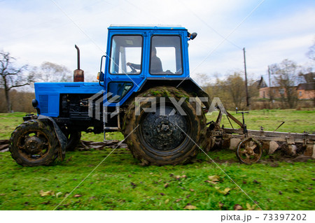 Land cultivation,tractor plows the ground, a blue small tractor and a plow with three knives. Land cultivation,tractor plows the ground, a blue small tractor and a plow with three knives. 73397202