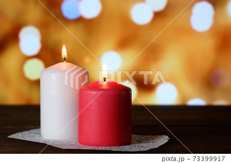 White and pink burning aromatic candles on white openwork paper napkin on wooden table, yellow bokeh lights background closeup view selective focus. Love, Valentine's, women's day, romantic concept 73399917