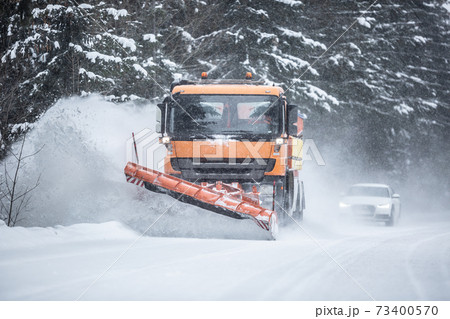 Snowplow clearing road from snow in the forest with traffic lining up behind the truck 73400570