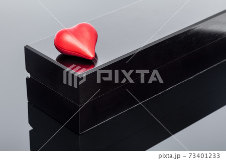 red shape volumetric heart lies on a black gift box on black glass with reflection, background on the theme of celebrating valentine's day. red shape volumetric heart lies on a black gift box on black glass with reflection, background on the theme of celebrating valentine's day. 73401233