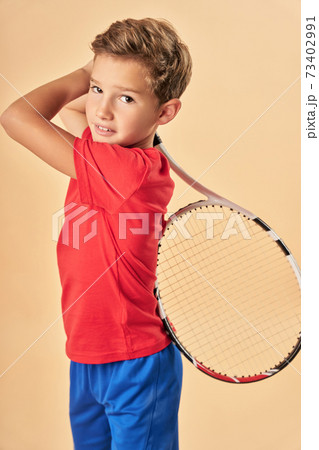Cute boy with tennis racket standing against light orange background 73402991