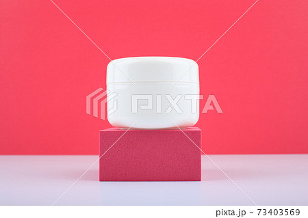 Close up of white glossy jar with cream, balm or hair or face mask on podium against bright pink background 73403569