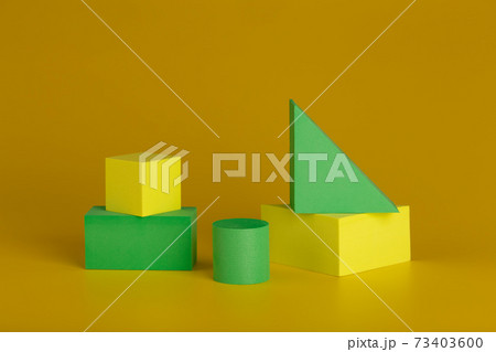 Duotone geometric still life with yellow and green figures against dark yellow background 73403600