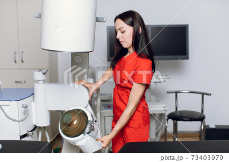 Portait of pretty confident focused Caucasian female doctor, wearing red medical uniform, working in modern clinic with ultrasonic lithotripter machine. Kidney stones treatment concept 73403979