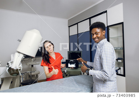 Happy doctor and patient in modern urology clinic. Young female doctor and her male african patient, holding tablet pc with ultrasound scan, smiling to camera and showing thumbs up 73403985