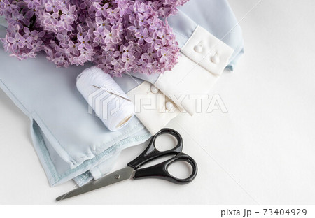 Old scissors, a spool of thread, a cloth and a branch of lilac shot in a nostalgic tone 73404929