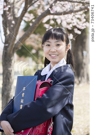 桜の前で卒業証書とランドセルを抱える制服姿の女子小学6年生 卒業イメージの写真素材