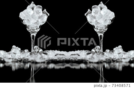Cocktail glass with ice inside and scattered outside on a black glossy background 73408571