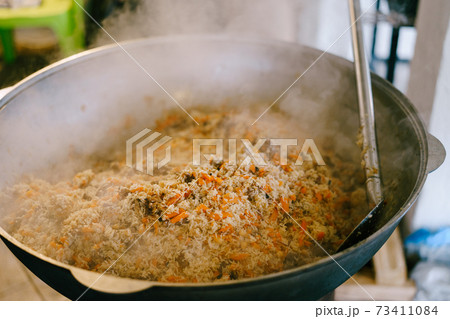 The cook stirs pilaf in the cauldron. 73411084