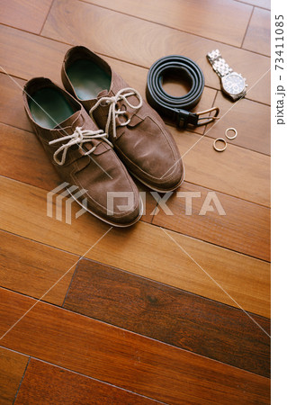 Top view of brown men's shoes with a wristwatch, belt and wedding rings of the bride and groom on a wooden texture. Top view of brown men's shoes with a wristwatch, belt and wedding rings of the bride and groom on a wooden texture. 73411085