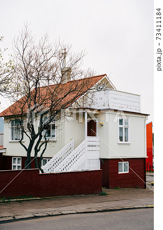 The house is cream-colored with an orange roof, white railings on the stairs before entering in Reykjavik, the capital of Iceland. 73411184