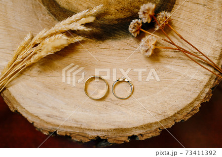 Gold wedding rings on a wooden cut with spikelets and dried flowers. 73411392