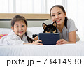 Happy Asian mother and daughter lying on bed and using digital tablet. Black Shiba Inu on bed between its owner. Concept family with dog at home. 73414930