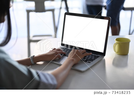 Close up view young woman hands typing on mock up laptop computer with blank screen at her workstation. Close up view young woman hands typing on mock up laptop computer with blank screen at her workstation. 73418235