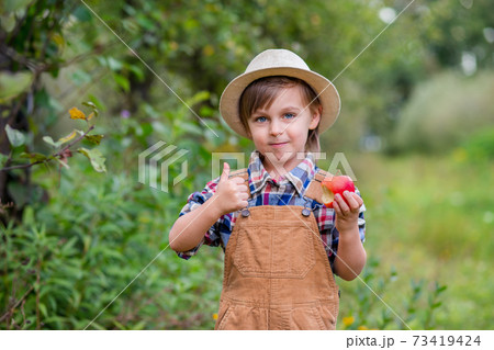 Portrait of one cute boy in a hat in the garden with a red apple, emotions, happiness, food. Autumn harvest of apples. Portrait of one cute boy in a hat in the garden with a red apple, emotions, happiness, food. Autumn harvest of apples. 73419424