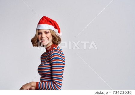 Happy woman in a Christmas cap and a striped sweater gestures with her hands for the New Year holidays Happy woman in a Christmas cap and a striped sweater gestures with her hands for the New Year holidays 73423036