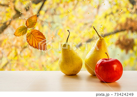 Apple, pears and autumn yellow leaf on window glass with water drops in the blurred background. 73424249